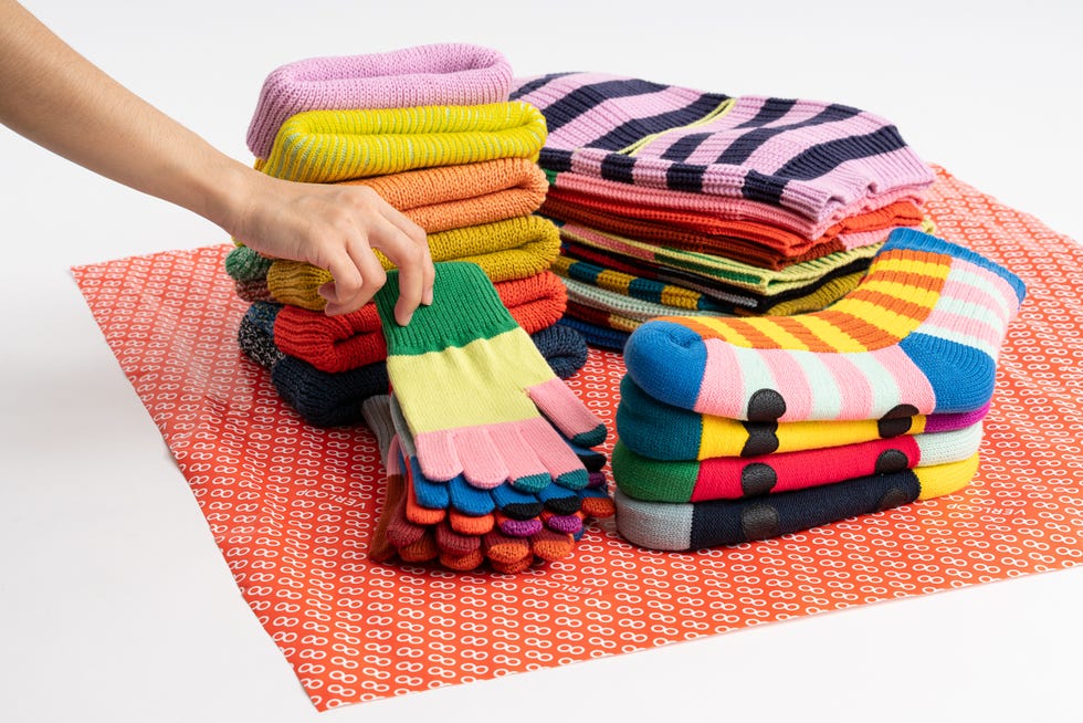 a person putting a colorful knitted hat on a pile of colorful yarn