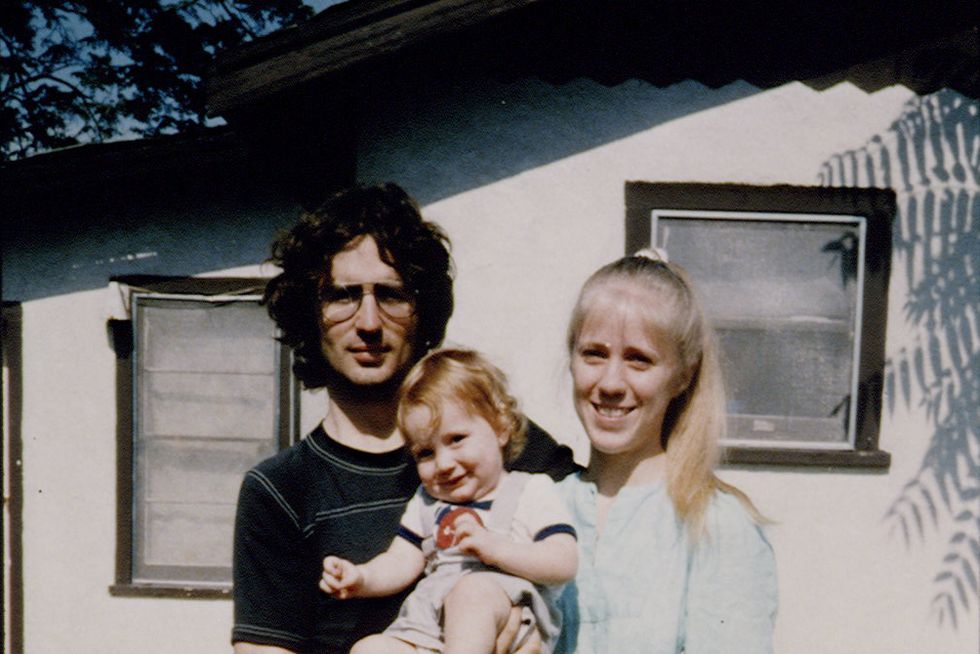 david koresh, wearing a black shirt and sunglasses, holds a smiling baby and stands next to a woman wearing a blue shirt