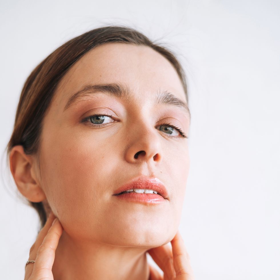 vertical beauty portrait of young woman with clear healthy skin and hands on her face against white backdrop