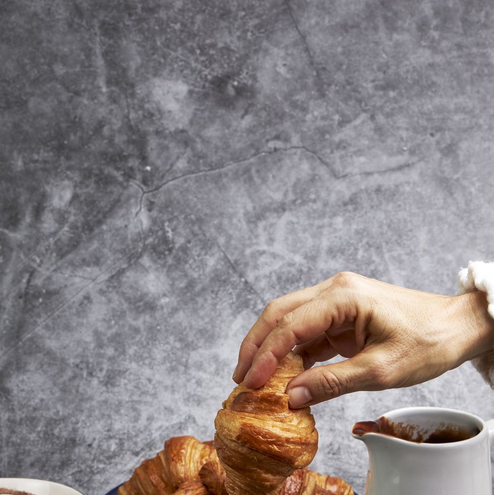 vertical image of hand of woman dropping a croissant into a cup of hot chocolate,spain