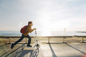 Boy riding scooter on beach promenade at sunset