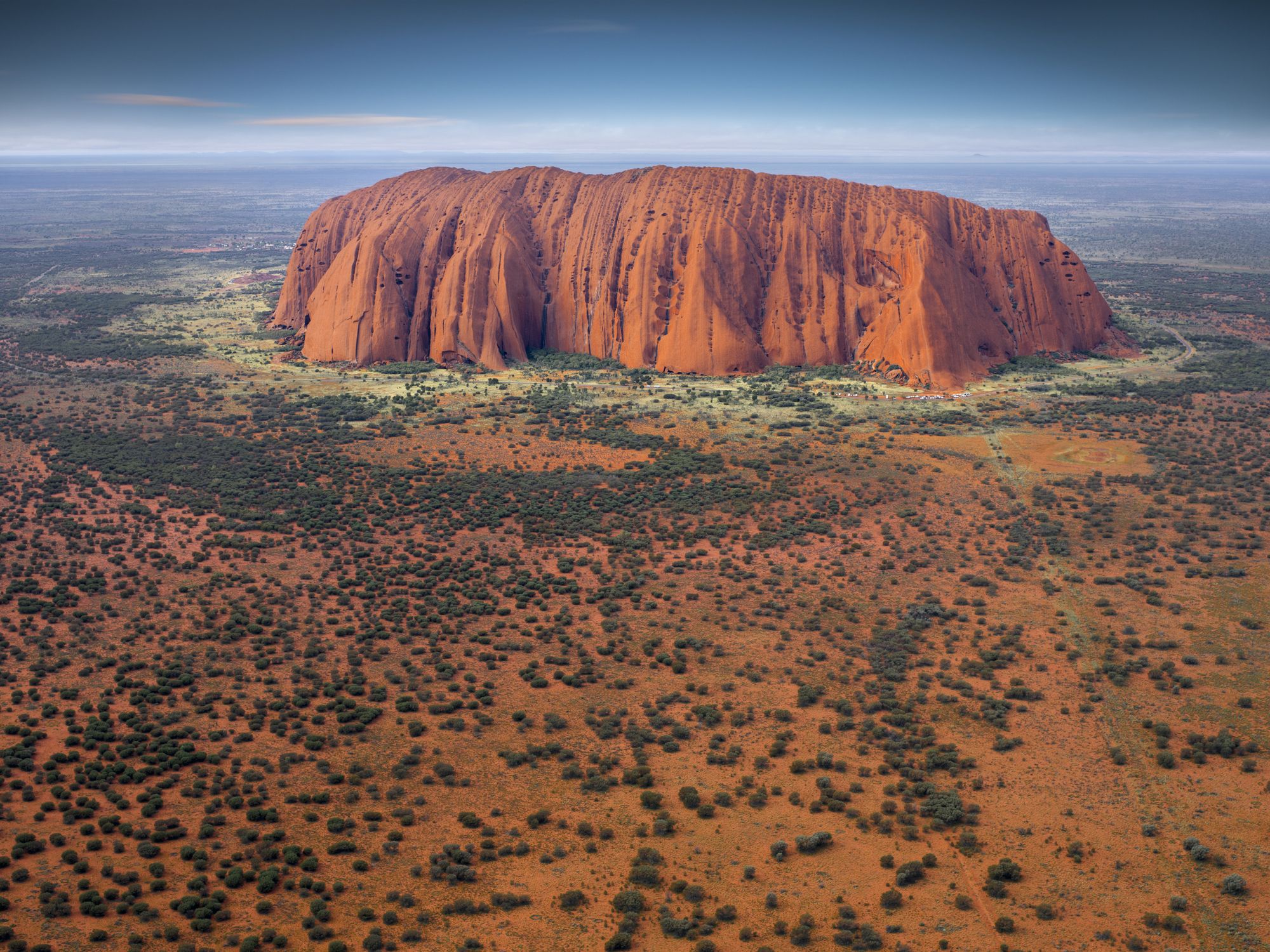 a large red rock formation with Uluru in the background
