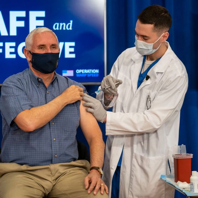 vice president pence is sitting down and hold his left sleeve shirt as a health care provided sticks a vaccination needle into his arm, both men are wearing face masks