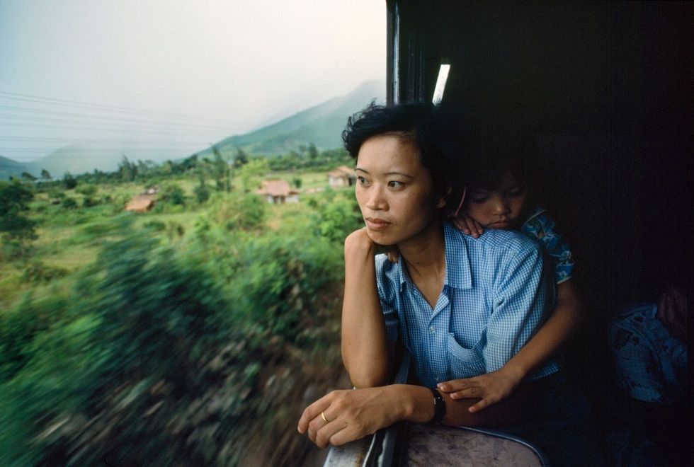 Diep Tran en haar kind genieten van de frisse lucht in de trein onderweg van Saigon naar Hanoi ook wel de Reunification Express genoemd 1990
