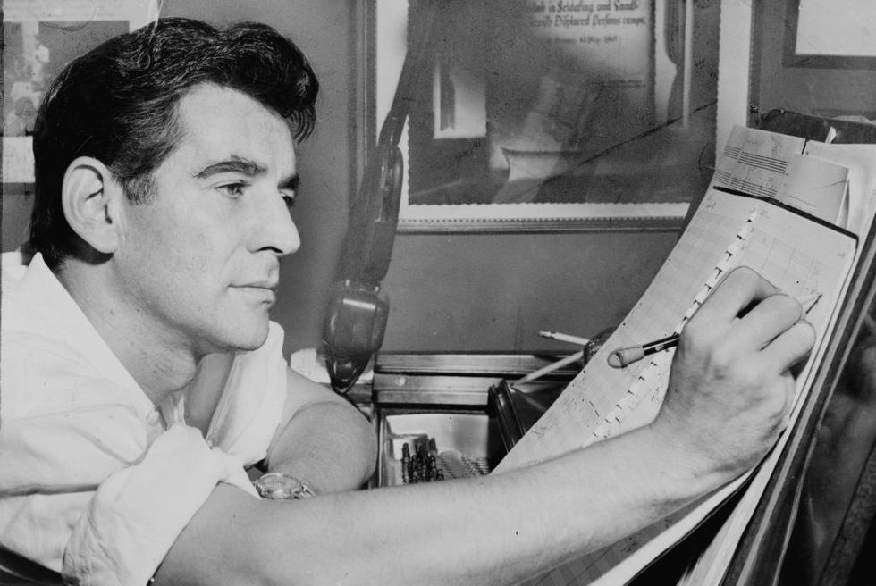leonard bernstein writing notations on a musical score while sitting at a piano