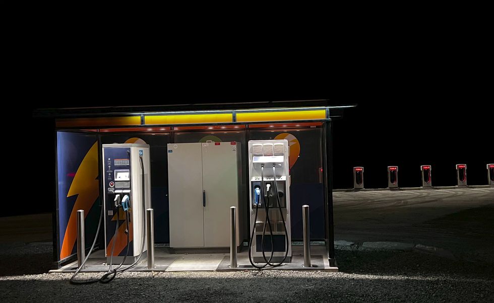 view of an electric charging station for electric cars with two electric chargers in the background more electric chargers in a row with a parking lot photograph taken at night