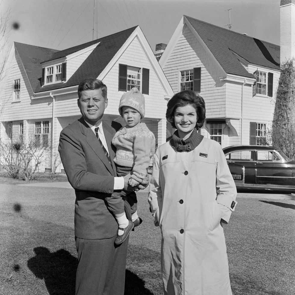 john f kennedy, caroline kennedy, and jacqueline kennedy look at the camera while outside a large house, john holds caroline