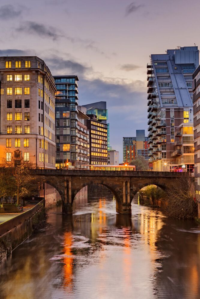 a bridge in manchester featuring brightly lit buildings and water under the bridge
