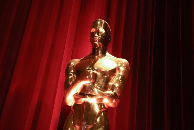 a close up photo of a gold oscar statuette with a red curtain behind it