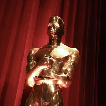 a close up photo of a gold oscar statuette with a red curtain behind it