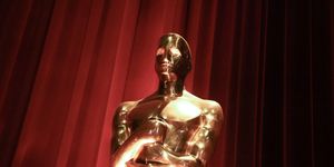 a close up photo of a gold oscar statuette with a red curtain behind it