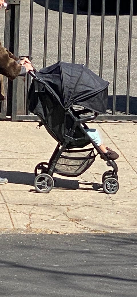 black stroller with a child inside being pushed by a parent down a street in brooklyn