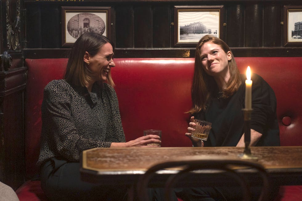 suranne jones as amy silva and rose leslie as kirsten longacre laughing and drinking sitting in a pub in vigil