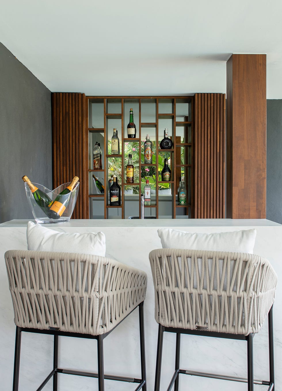 mueble bar con estantes de madera y barra tipo mármol con taburetes