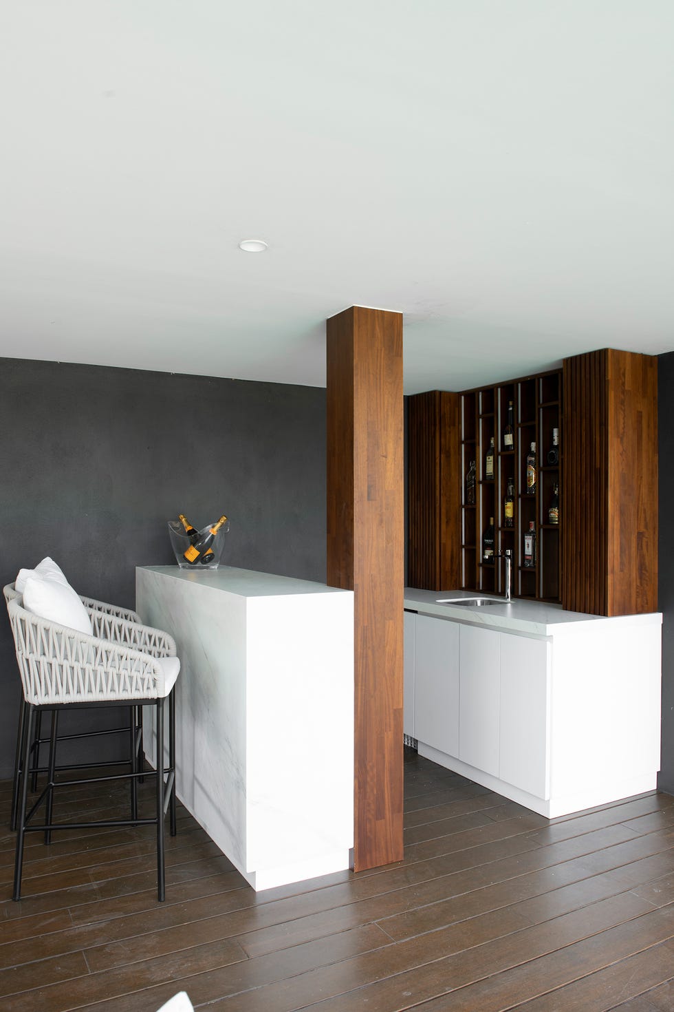 mueble bar con estantes de madera y barra tipo mármol con taburetes