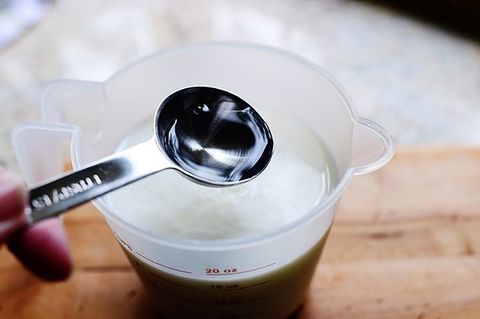 vinegar in measuring spoon with buttermilk in measuring cup