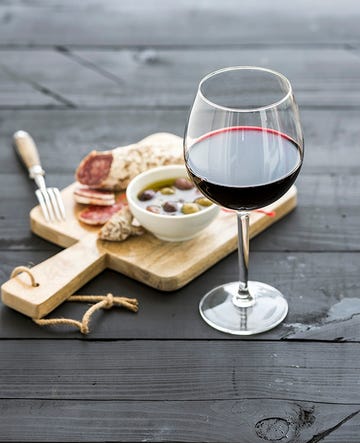 wine appetizer set glass of red wine, french sausage and olives on black wooden backdrop, selective focus, vertical composition