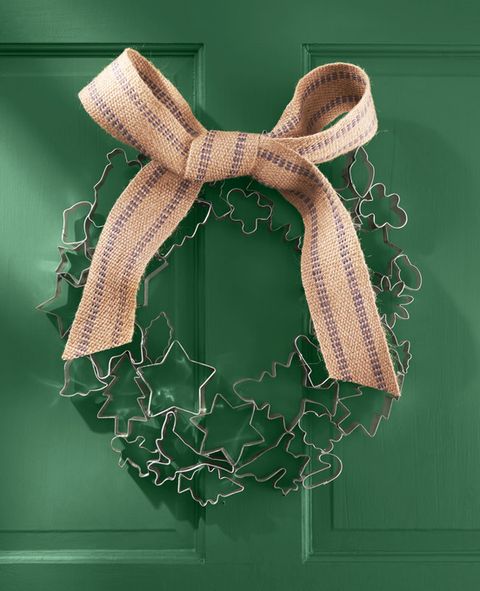 a wreath made of vintage cookie cutters and a burlap bow hangs on a green door