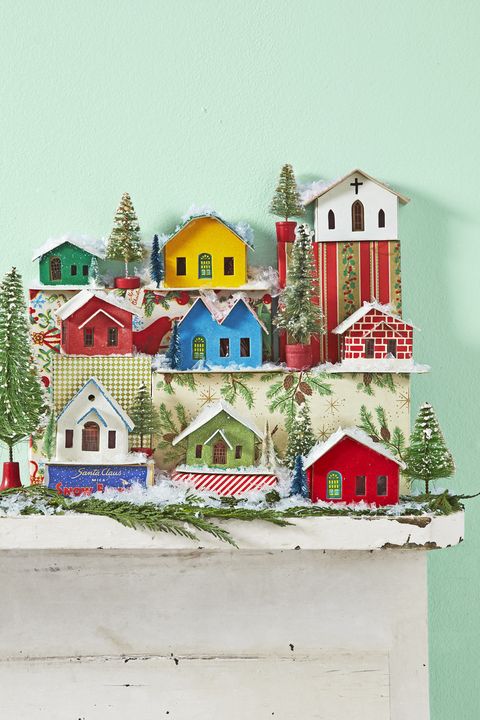 colorful tiny cardboard houses called putz houses are arranged on a mantel