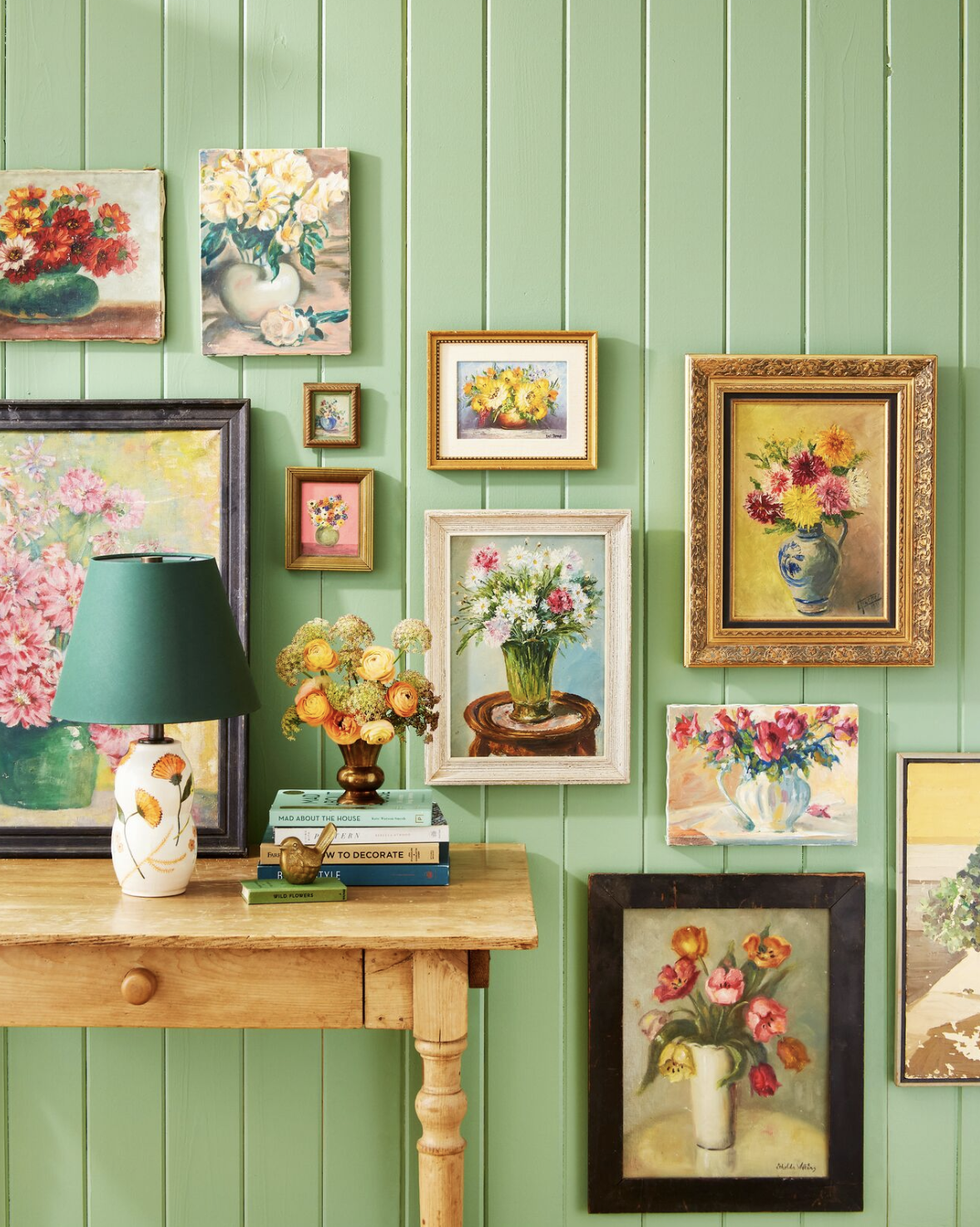 collection of vintage floral paintings displayed on a green beadboard wall