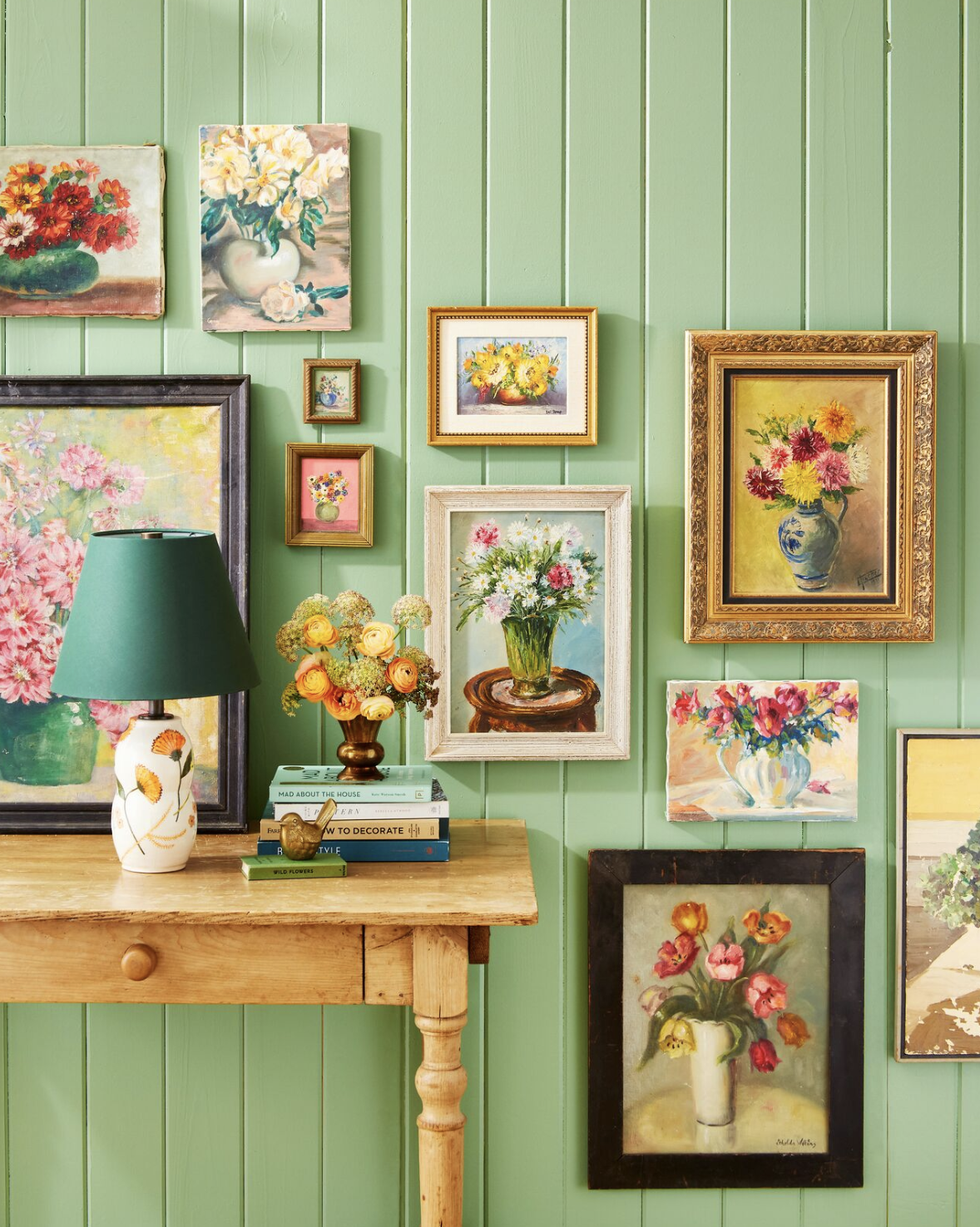collection of vintage floral paintings displayed on a green beadboard wall