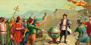vintage color illustration of christopher columbus standing on a ship deck with one hand on a large globe and the other on his hip holding a paper scroll, he wears a hat, dark jacket, long sleeve shirts, dark pants and leggings, several people surround him on the deck many with their hands out toward him