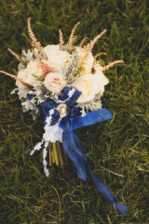 beautifully decorated brides bouquet of different white, beige, pink roses, green leaves, decorative ornaments, tied with a bright blue satin ribbon, lies on the autumn grass wedding theme