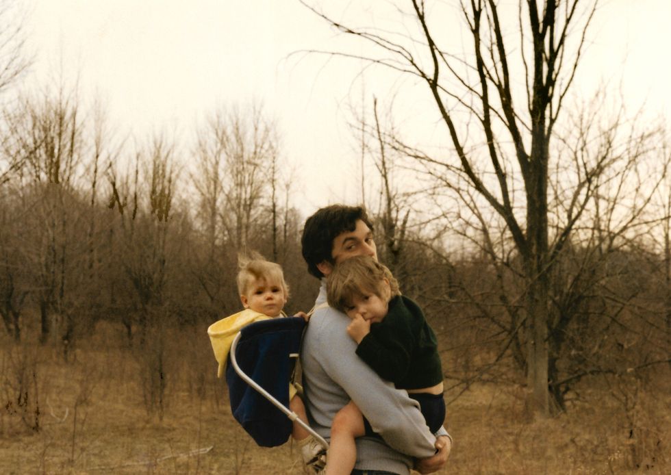 vintage late 1960s photo of young dad carrying kids on a walk in the woods