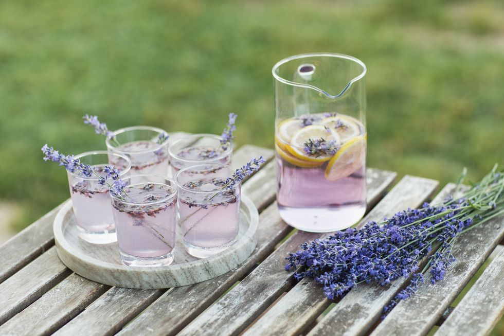 violet lavender cocktail decorated with flowers on wooden table outdoor