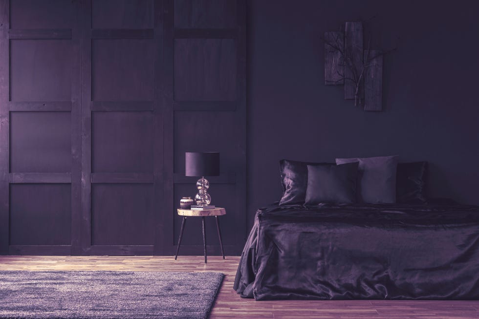 lamp on wooden table in spacious violet bedroom interior with decor above bed