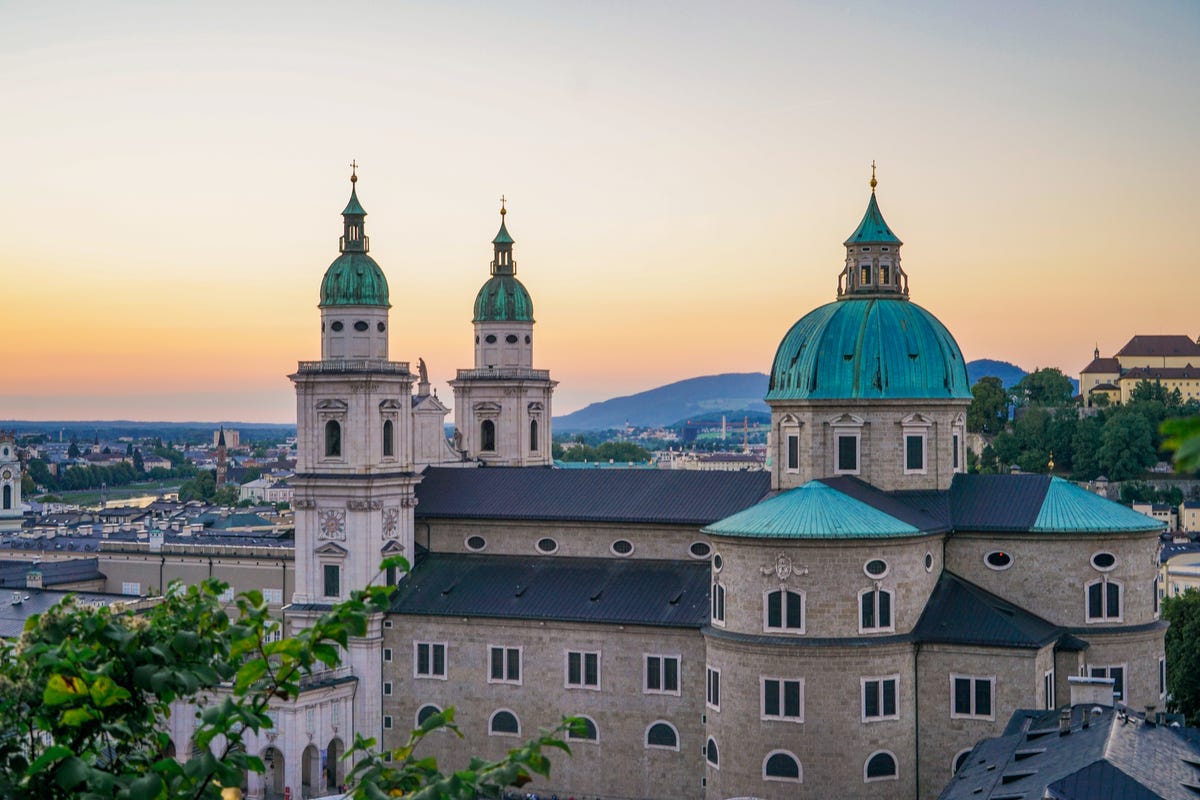 a sunset view of the exterior of the iconic salzburg cathedral in old salzburg, austria the sunset sky is visible in the background towers of the cathedral, and some buildings of old salzburg town are visible in the foreground