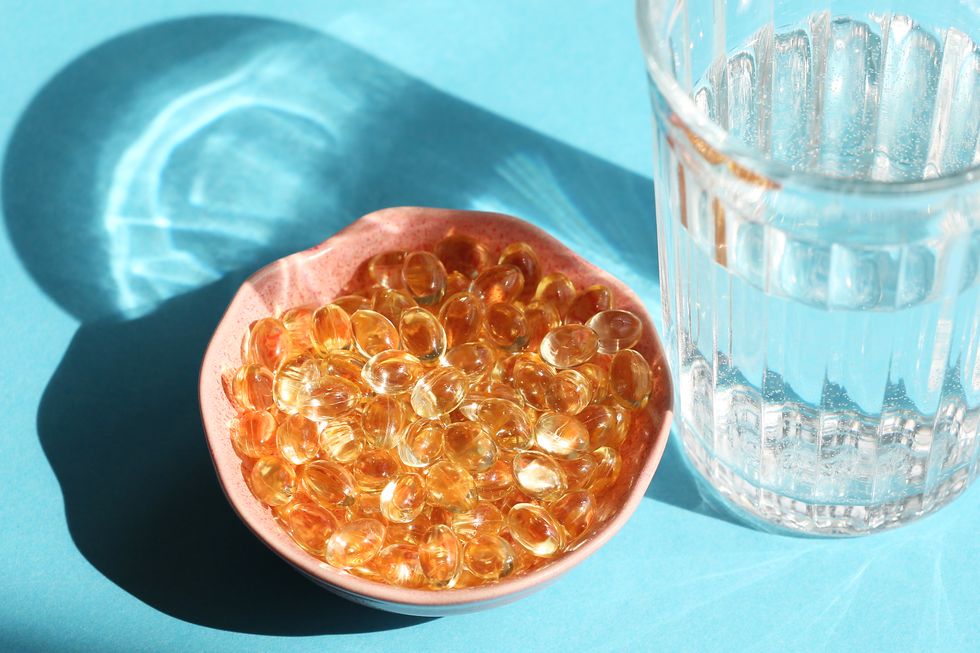 vitamin d capsules next the glass of water on blue background