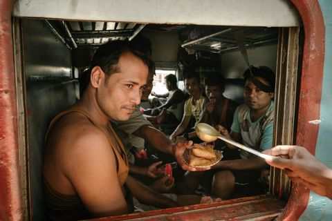 Door de raampjes van een tweedeklascoup worden passagiers bediend met een maaltijd van samosas Voor verkopers is het vaak eenvoudiger om gerechten van buitenaf te serveren dan om door de overvolle trein te lopen
