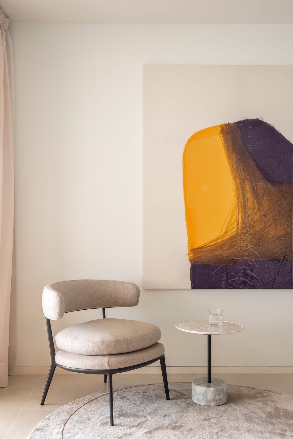 butaca beige, mesa auxiliar de mármol y cuadro abstracto en la pared