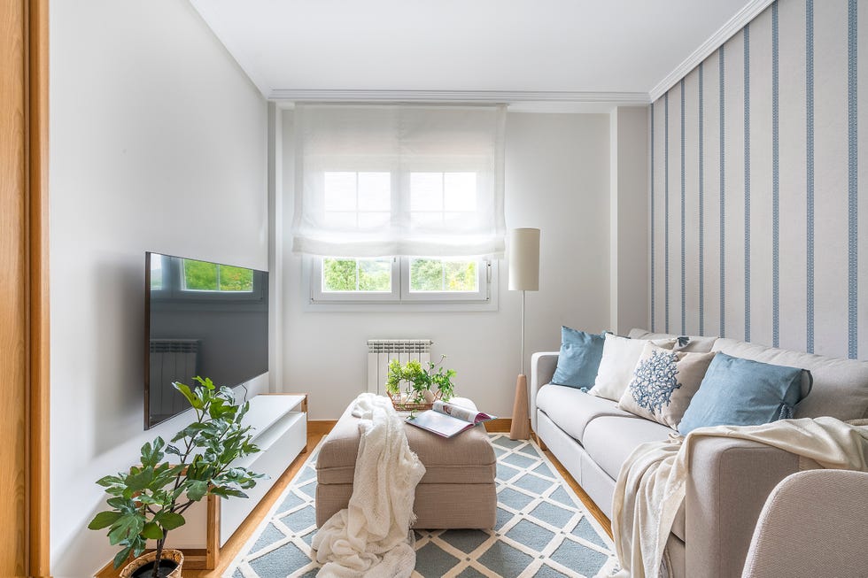 salón con papel pintado a rayas beige y azules, sofá beige y reposapiés a juego