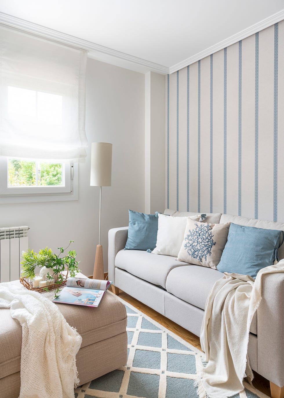 salón con papel pintado a rayas beige y azules, sofá beige y reposapiés a juego