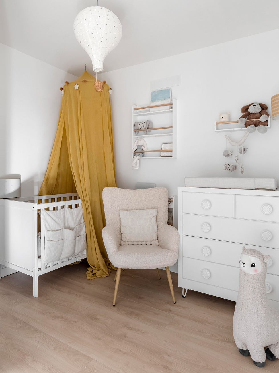 habitación de bebé con dosel mostaza en la cuna y butaca beige