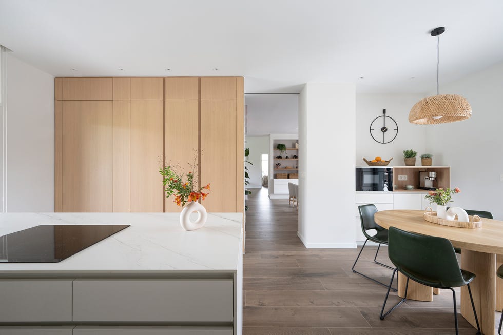 cocina abierta con isla y mesa de comedor de madera redonda con sillas de piel y lámpara de fibras