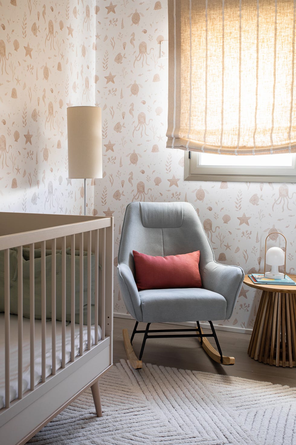 dormitorio infantil con mecedora, mesa auxiliar de madera redonda, cuna y papel pintado con motivos marinos