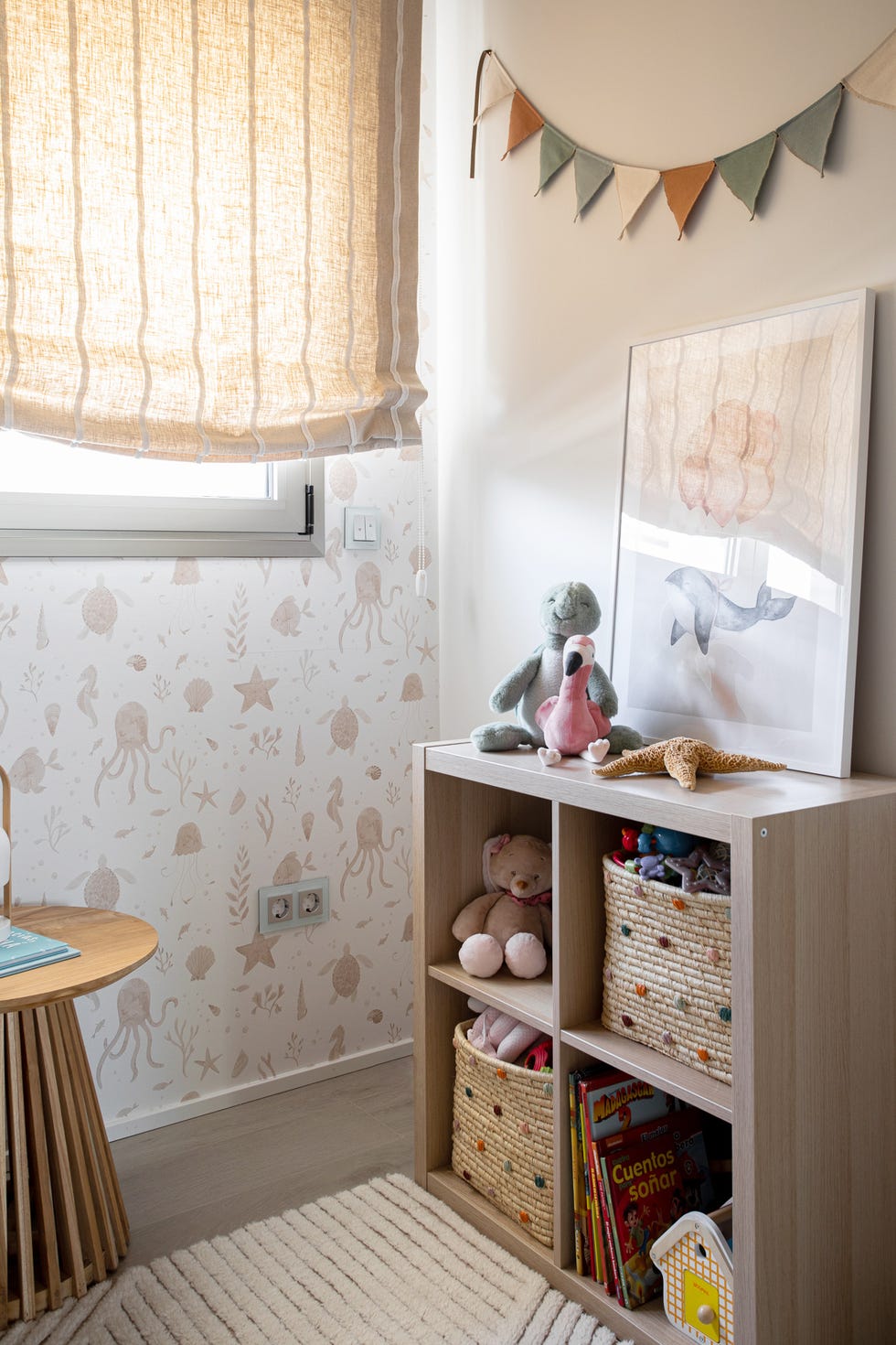 dormitorio infantil con mesa auxiliar de madera redonda, librería baja de madera y papel pintado con motivos marinos