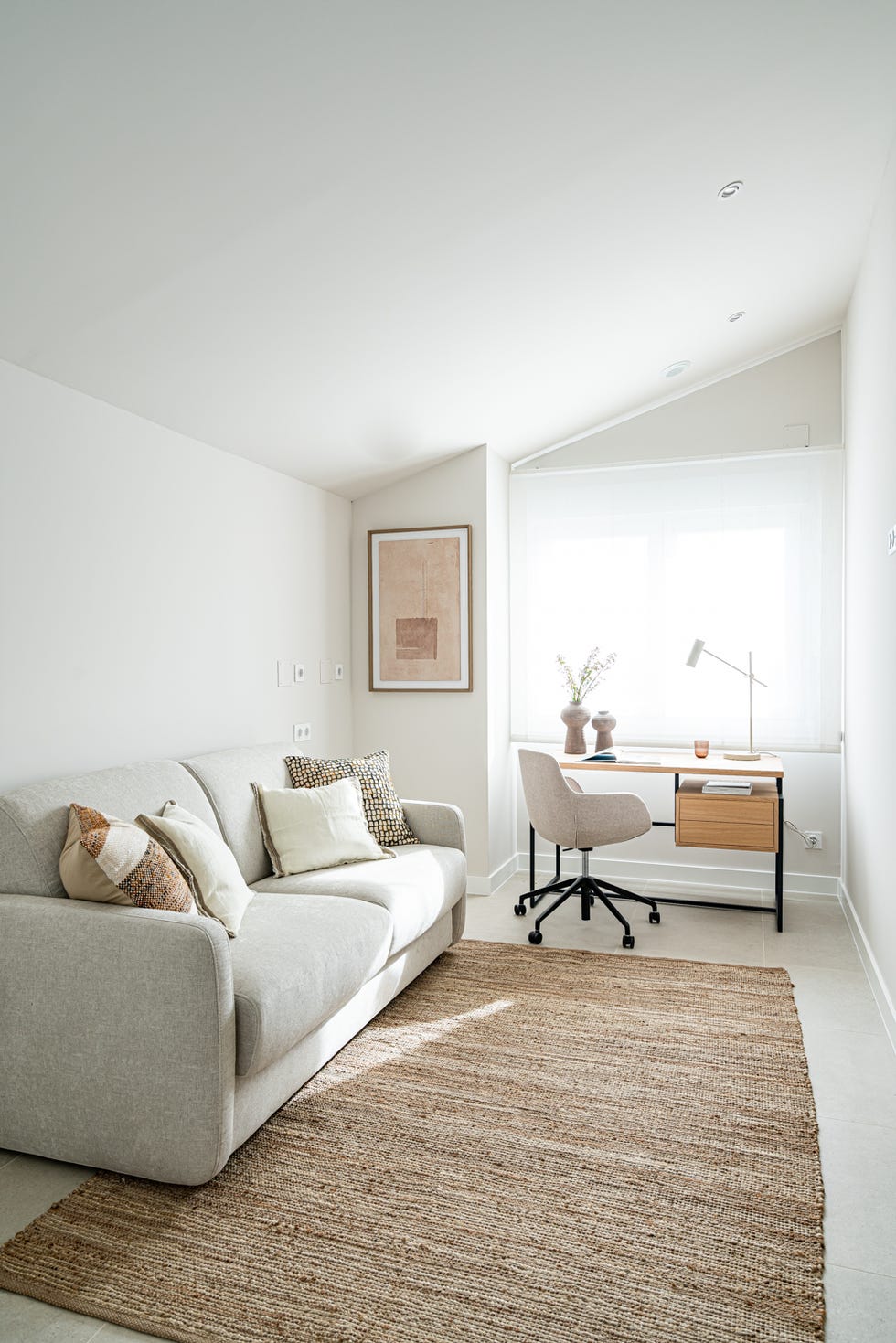 habitación con sofá cama gris, alfombra de yute y escritorio