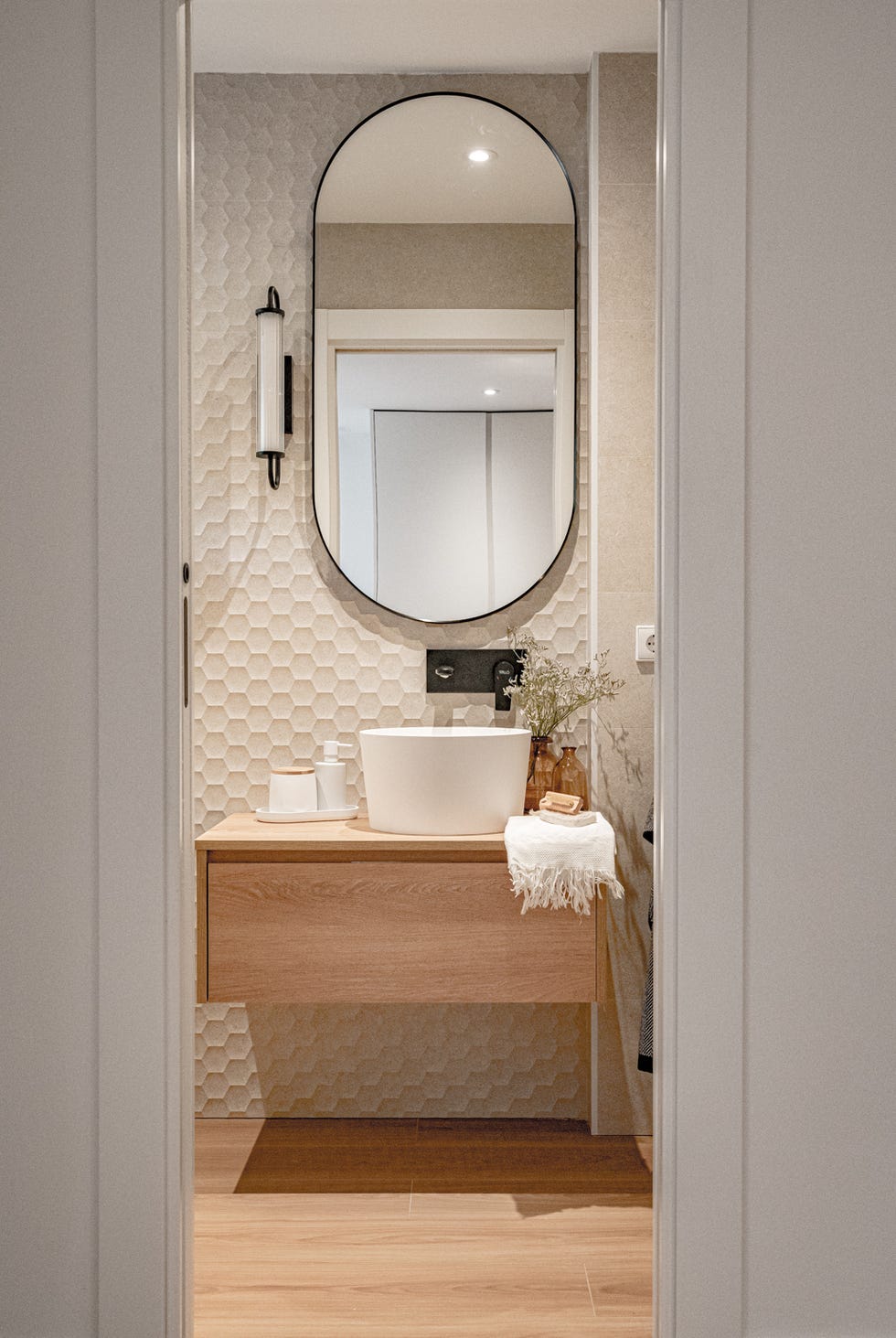 aseo con mueble de madera volado y pared de azulejos blancos con formato hexagonal