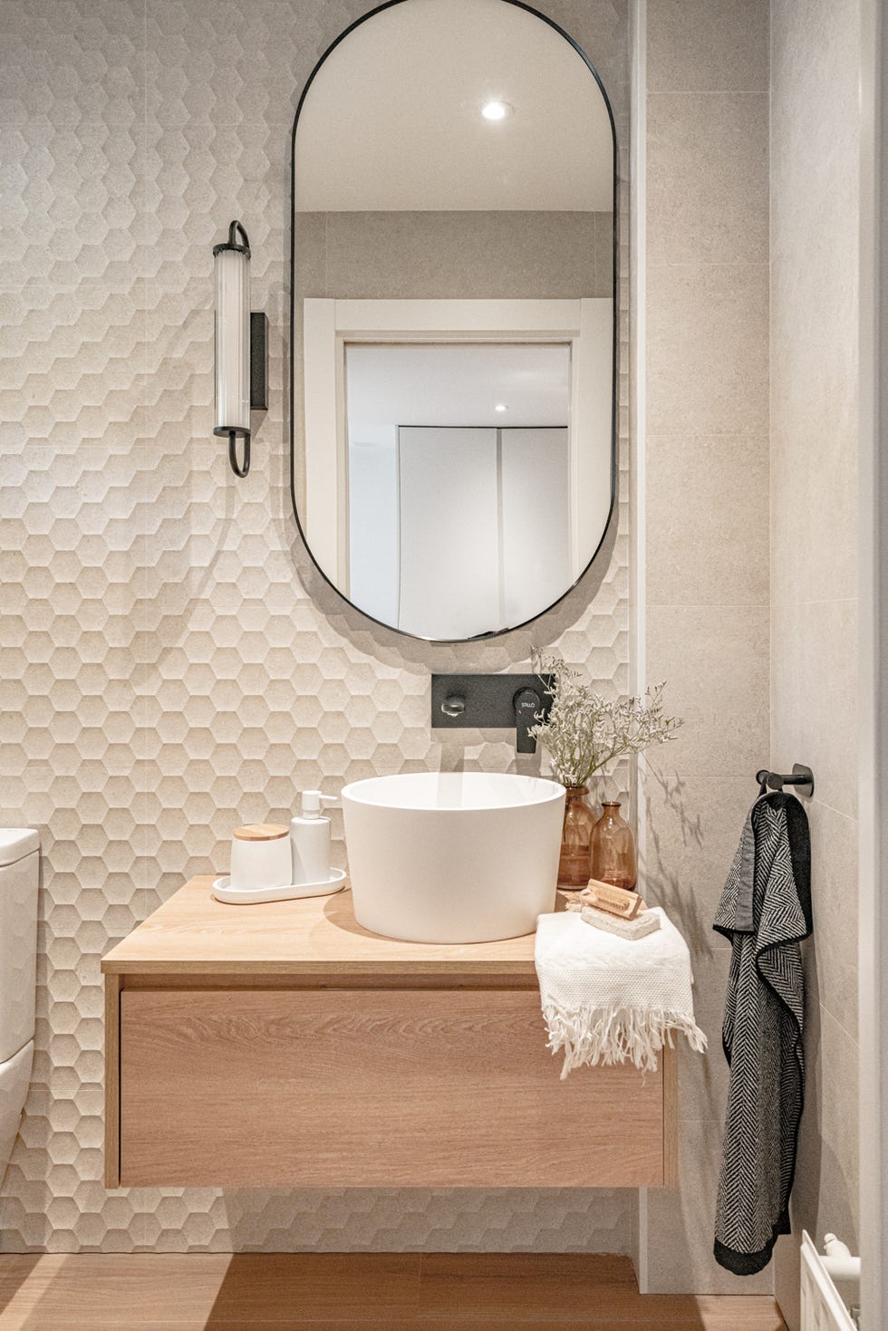 aseo con mueble de madera volado y pared de azulejos blancos con formato hexagonal