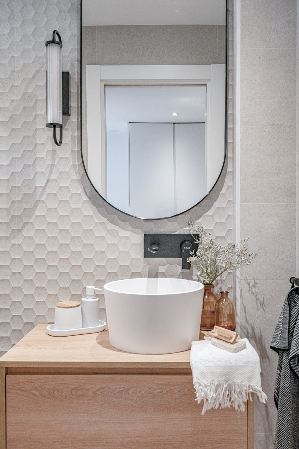 aseo con mueble de madera volado y pared de azulejos blancos con formato hexagonal