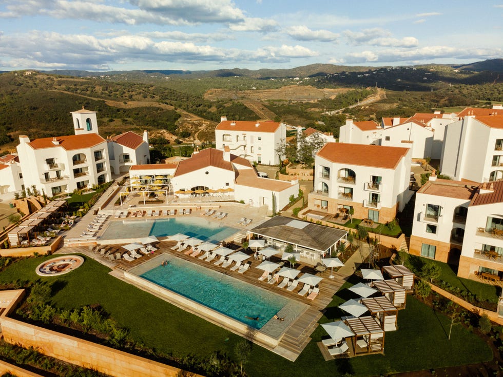 resort with a large swimming pool surrounded by lounge chairs and accommodation buildings in a scenic setting