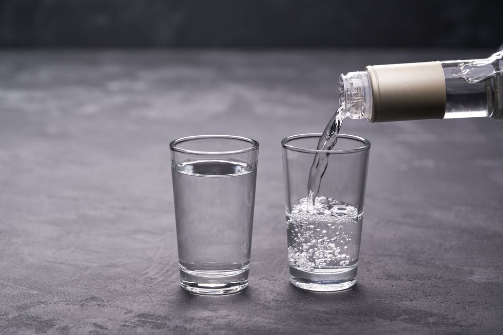 vodka from the bottle is poured into a glass on a black background, selective focus
