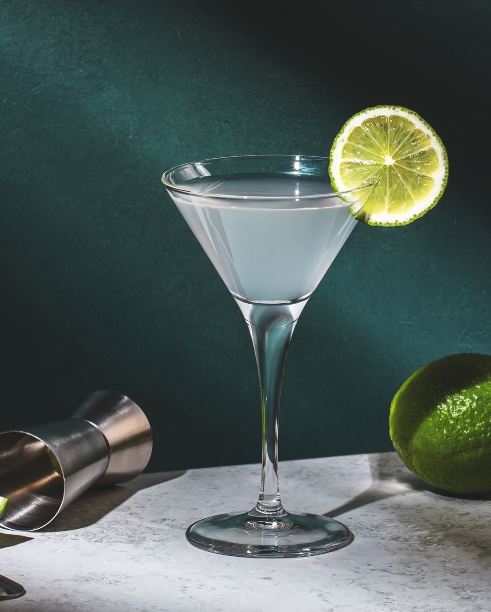 vodka gimlet alcoholic cocktail drink with vodka, syrup, lime juice and ice, dark green background, bright hard light and shadow pattern, banner