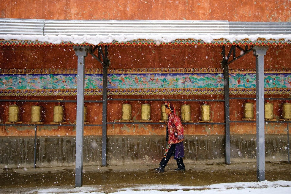 Een dorpeling loopt langs gebedsmolens in de Lai Shitempel een boeddhistisch heiligdom op het besneeuwde platteland van Yunnan
