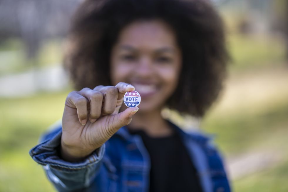 young woman holding up a "vote" button