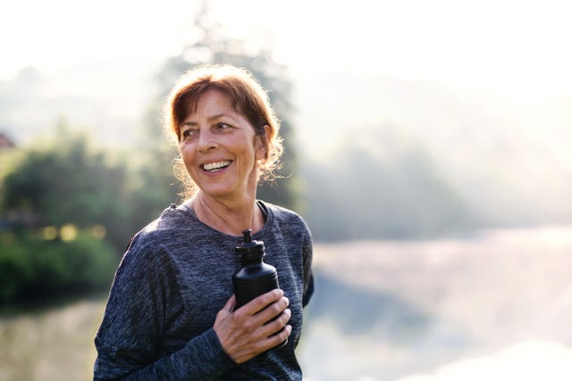 an old female sportsperson with black plastic water bottle doing sport outside in the countryside